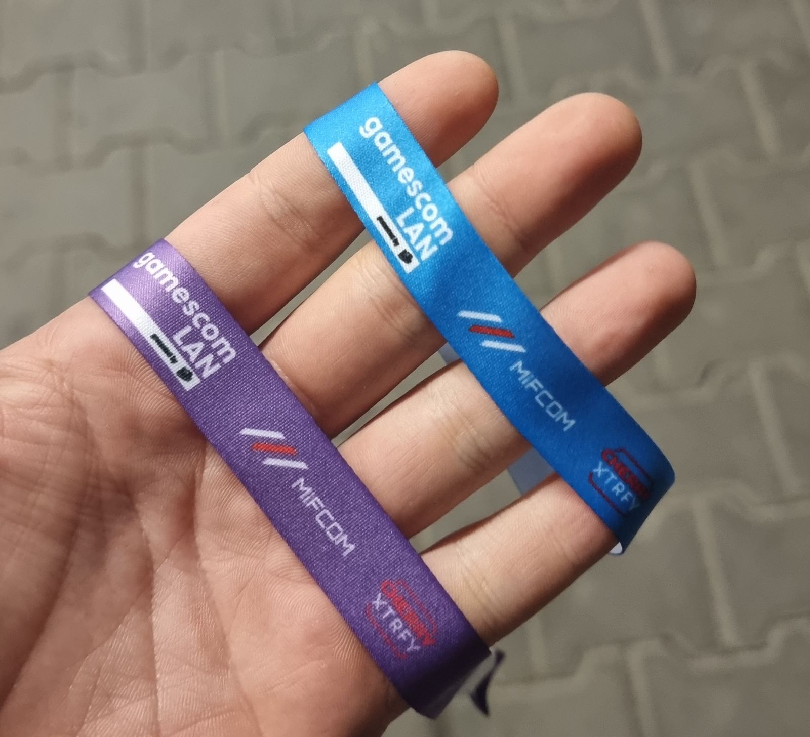 Zwei Stoffbändchen der gamescom LAN in Violett und Blau in einer geöffneten Hand